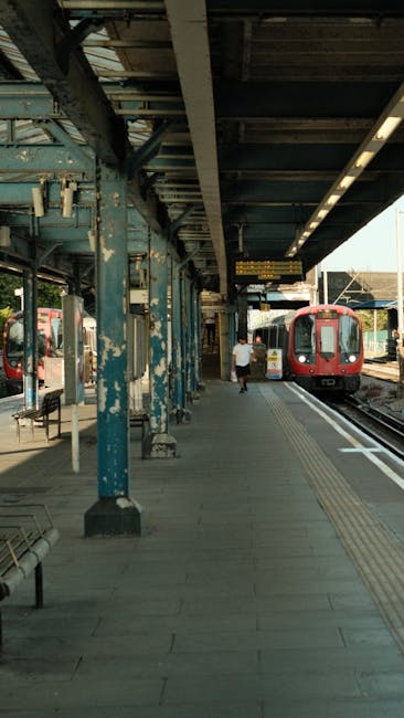 A covered platform at Kennington station featuring a concrete floor and blue-painted steel columns supporting a weathered, corrugated metal roof. The platform is clean and free of litter, with tactile